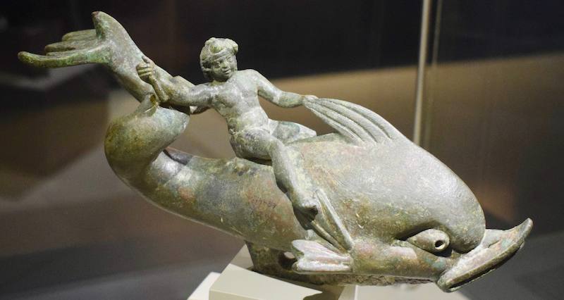 Estatuilla de bronce de un Eros tumbado sobre el lomo de un delfín en una vitrina